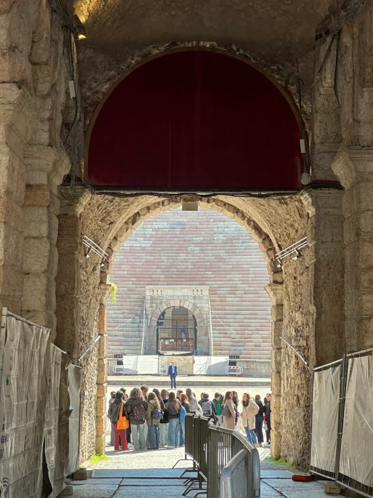 View through a stone archway inside the Arena di Verona showing visitors gathered near the entrance and the amphitheater seating in the background.