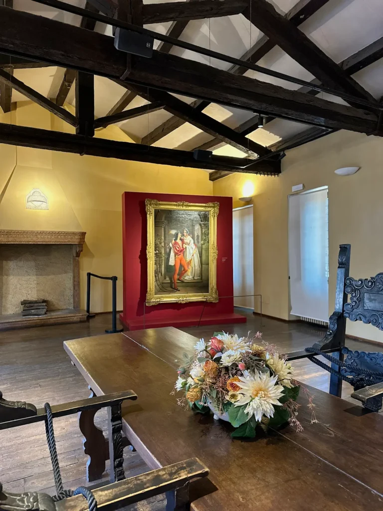Interior room inside Juliet's House Verona museum showing historic furniture and a Romeo and Juliet painting display.