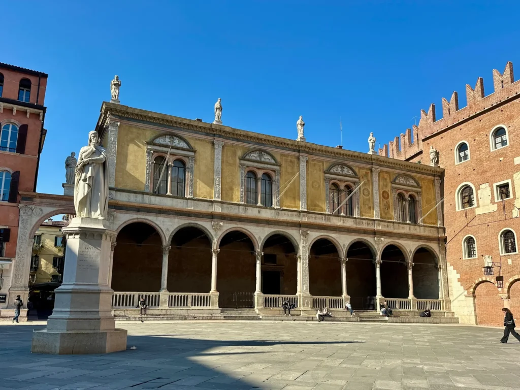 Piazza dei Signori Verona with the Loggia del Consiglio and Dante statue under a clear blue sky.