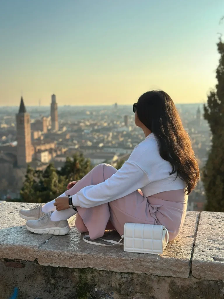 Castel San Pietro Verona viewpoint woman sitting on stone wall overlooking rooftops and Adige River at sunset