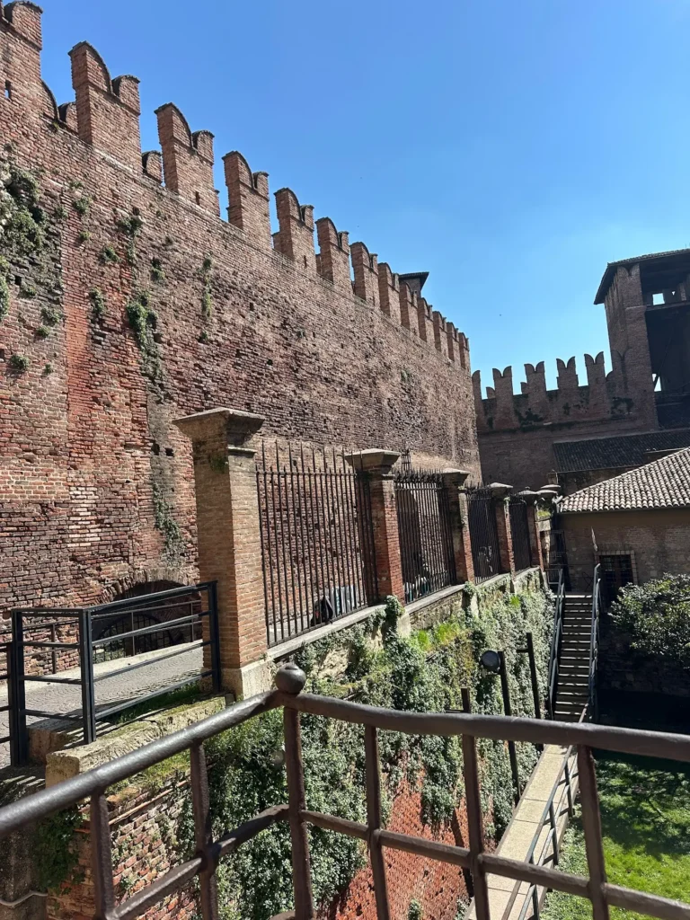 Castelvecchio Verona fortress walls with iron railings, towers, and layered brick structures under a clear sky.