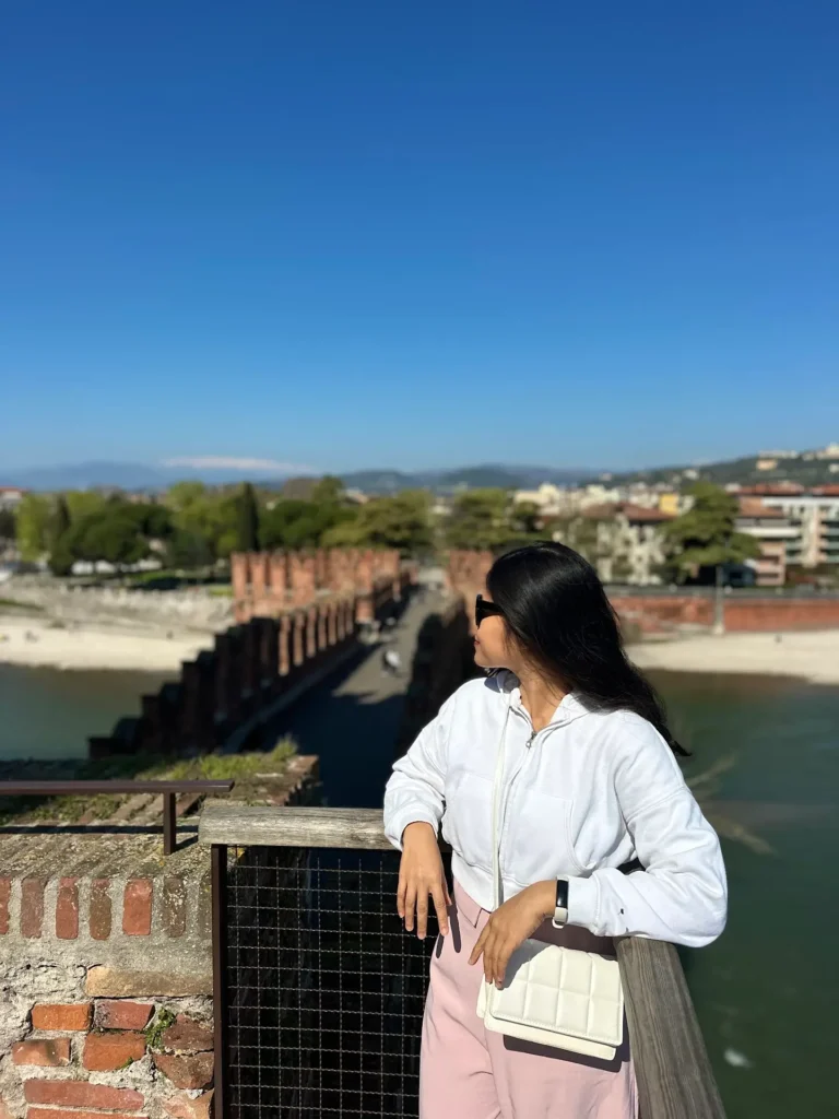 Castelvecchio Verona bridge close-up with a woman leaning on a railing and the fortress bridge blurred in the background.
