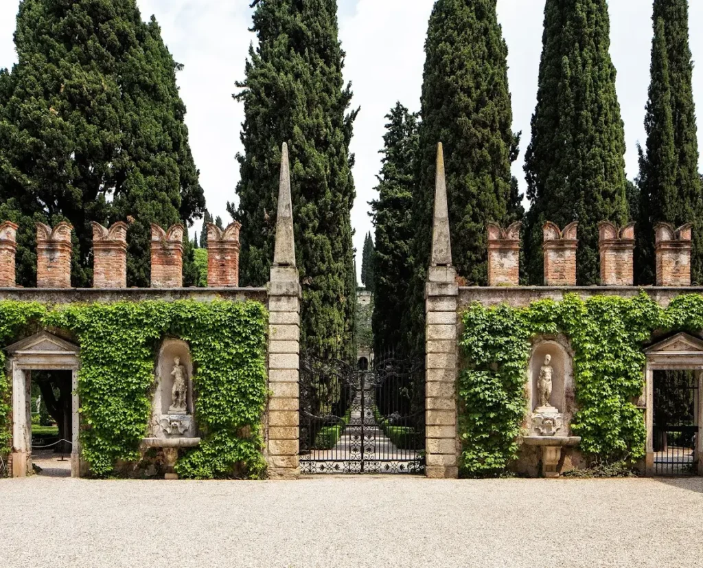The elegant entrance to Giardino Giusti in Verona, Italy, framed by towering cypress trees and ivy-covered stone walls.