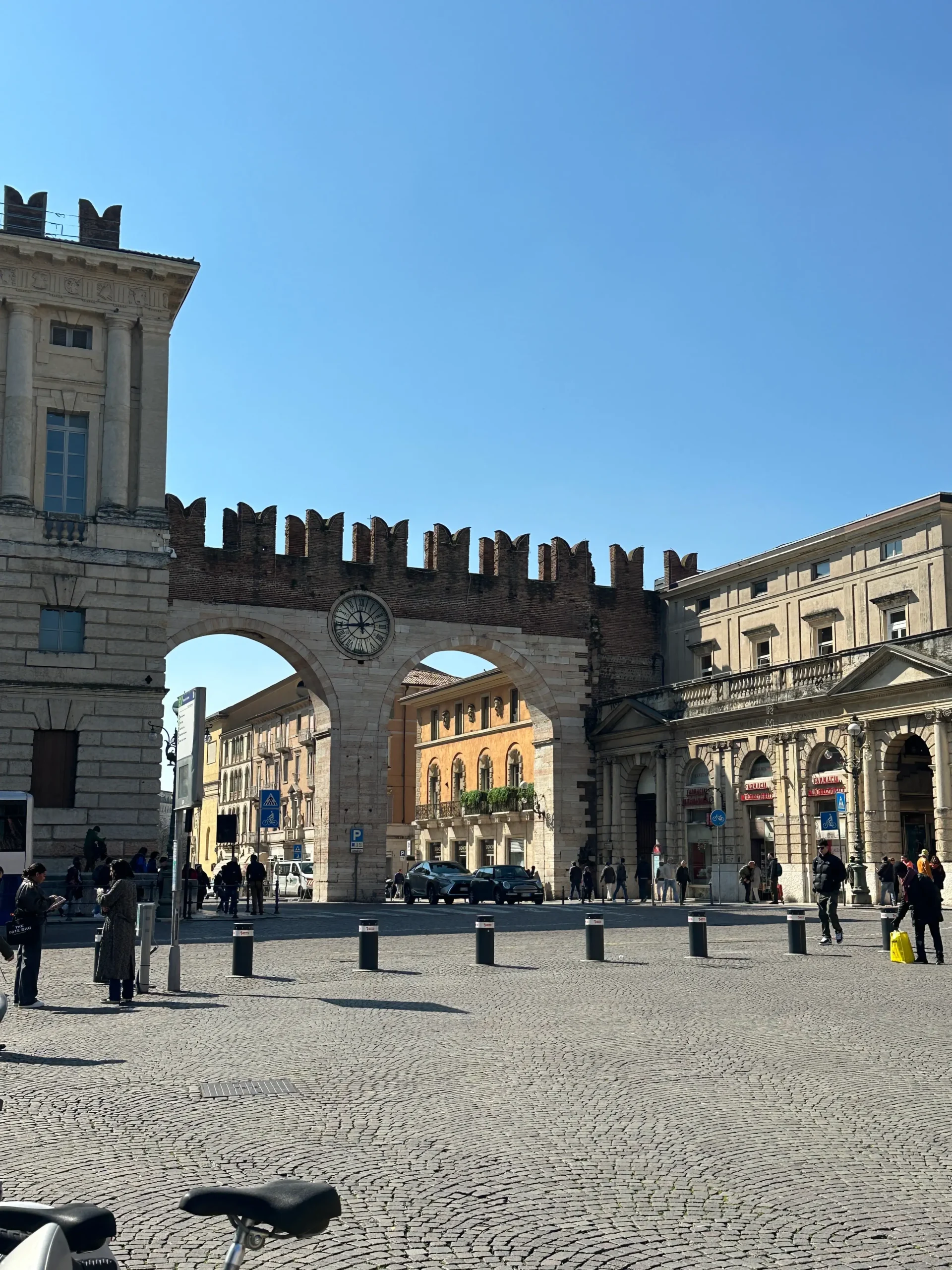 Historic archway and clock tower in Verona’s Piazza Bra with cobblestone square and surrounding buildings