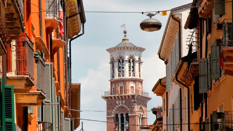 A narrow street in Verona, Italy, framed by colorful buildings with green shutters and balconies.
