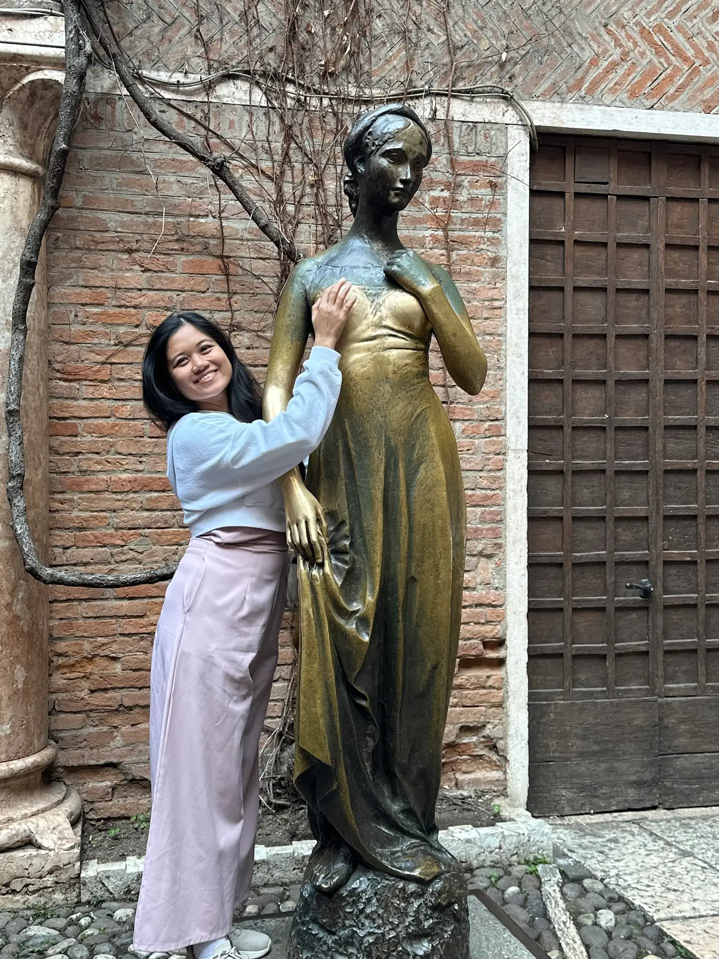 Visitor touching the bronze Juliet statue at Juliet's House Verona courtyard, a tradition believed to bring luck in love.