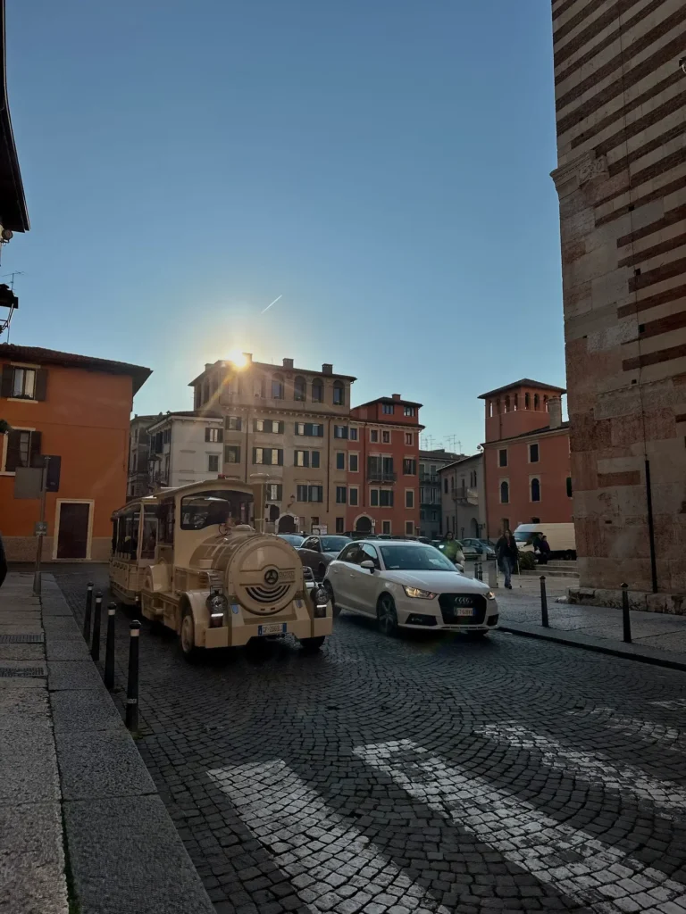 Day trips from Verona street scene with a tourist train passing historic buildings at sunset in Verona, Italy