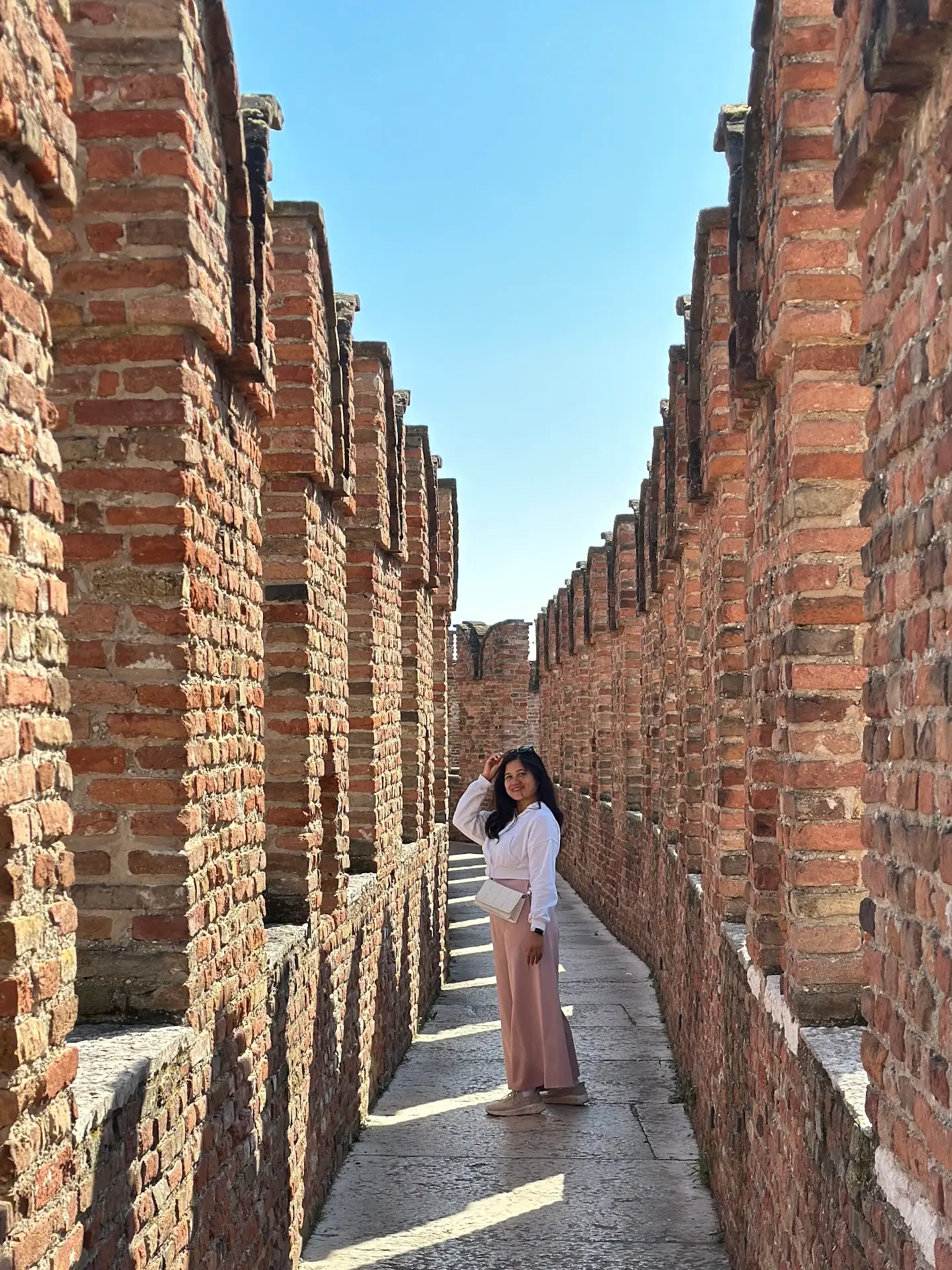 Castelvecchio Verona walkway with red brick crenellated walls and a woman standing along the narrow path.
