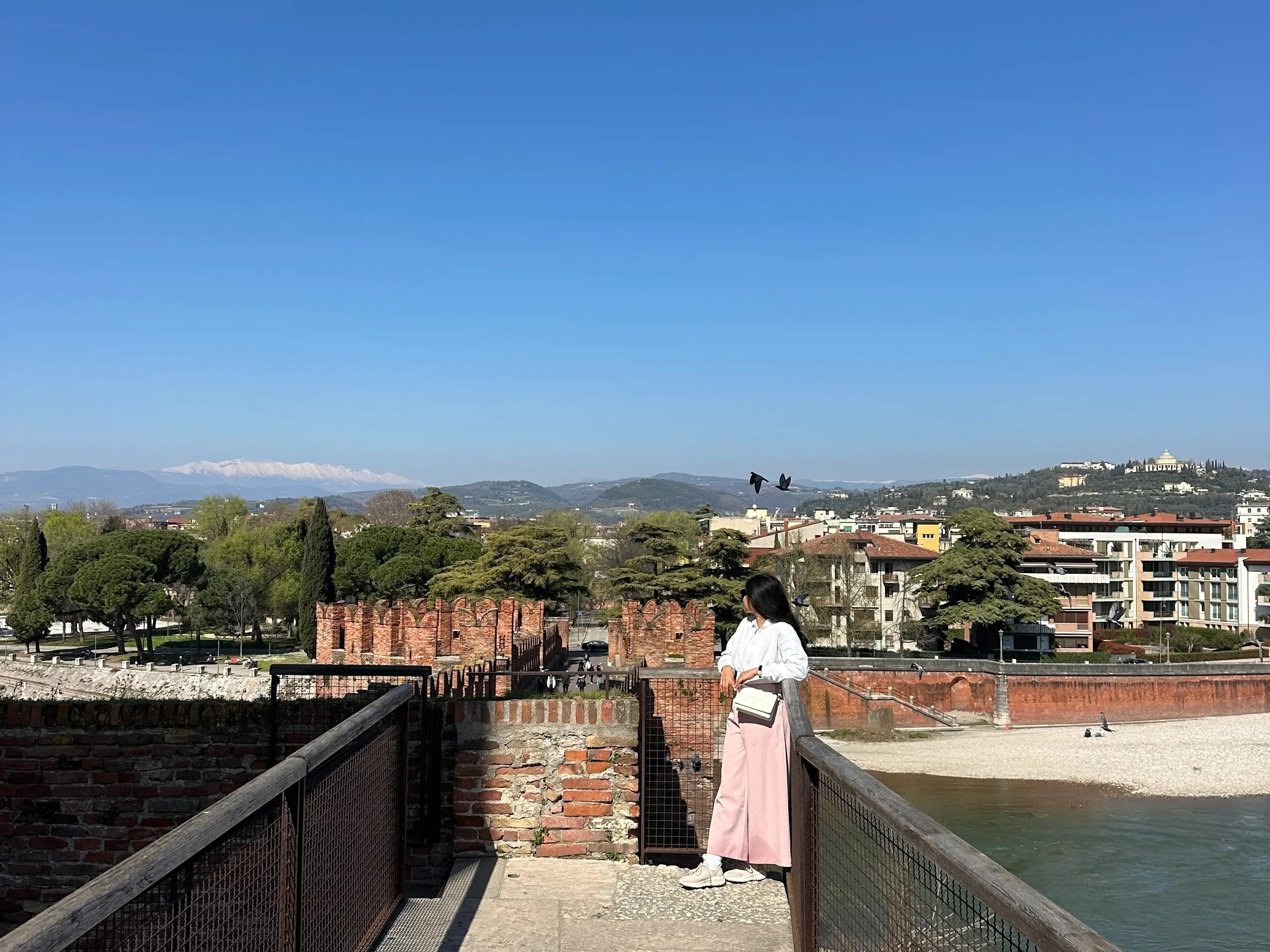 Castelvecchio Verona bridge viewpoint with a woman standing by the railing overlooking the river and city.